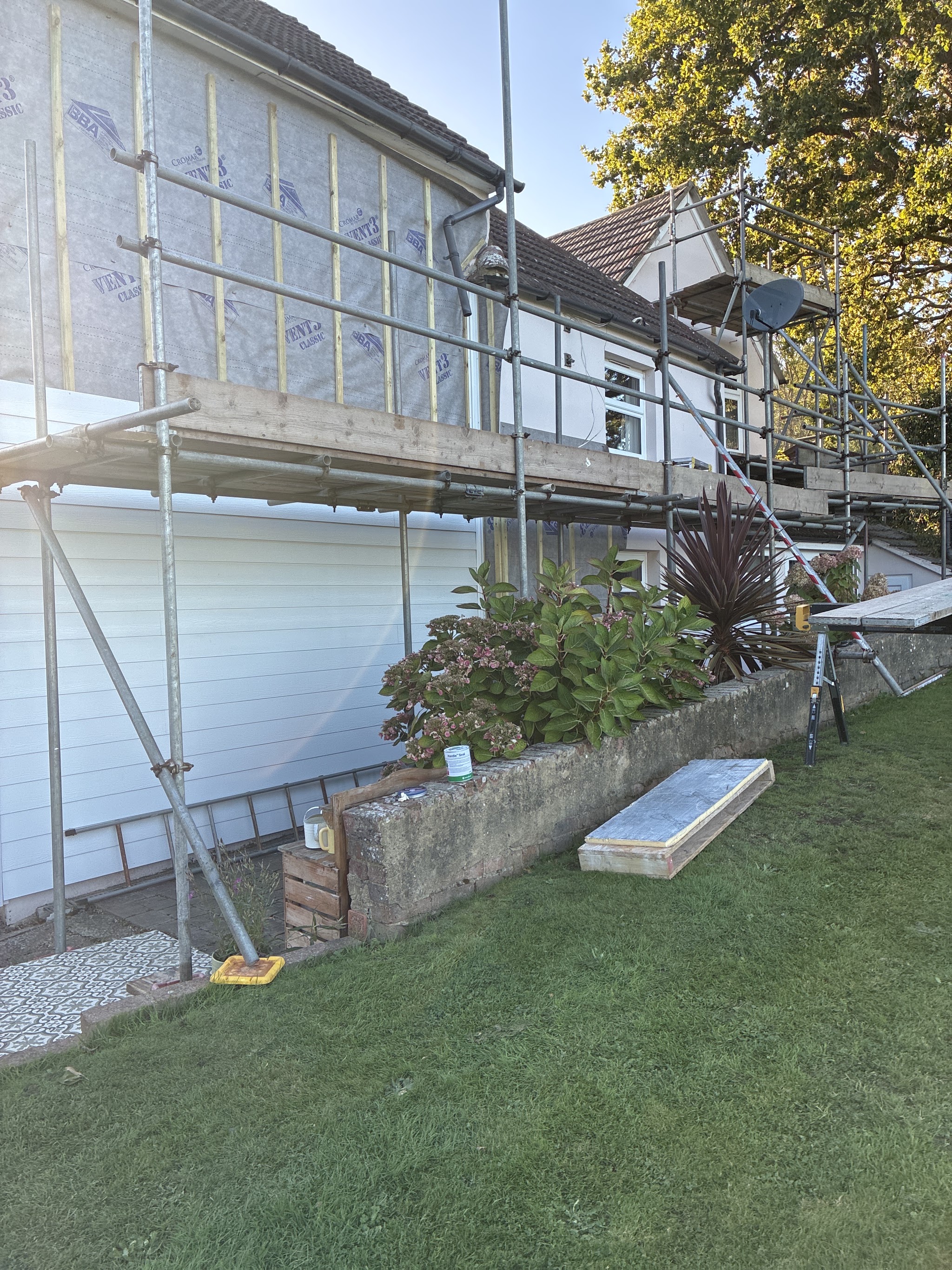 Scaffold along the side of a weatherboarded house above a garden