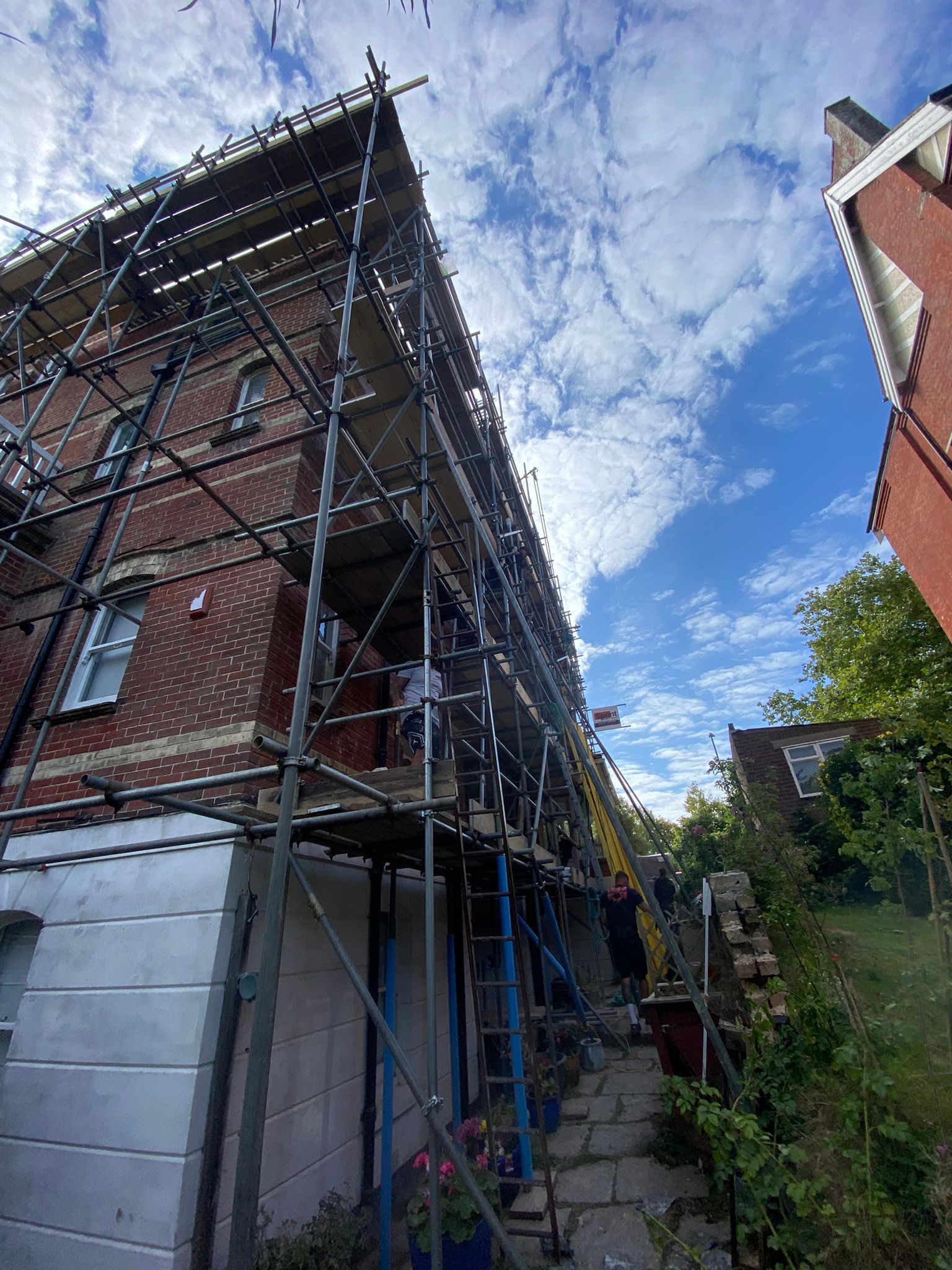 Looking up a full-height scaffold on a tall red-brick terrace against a blue sky
